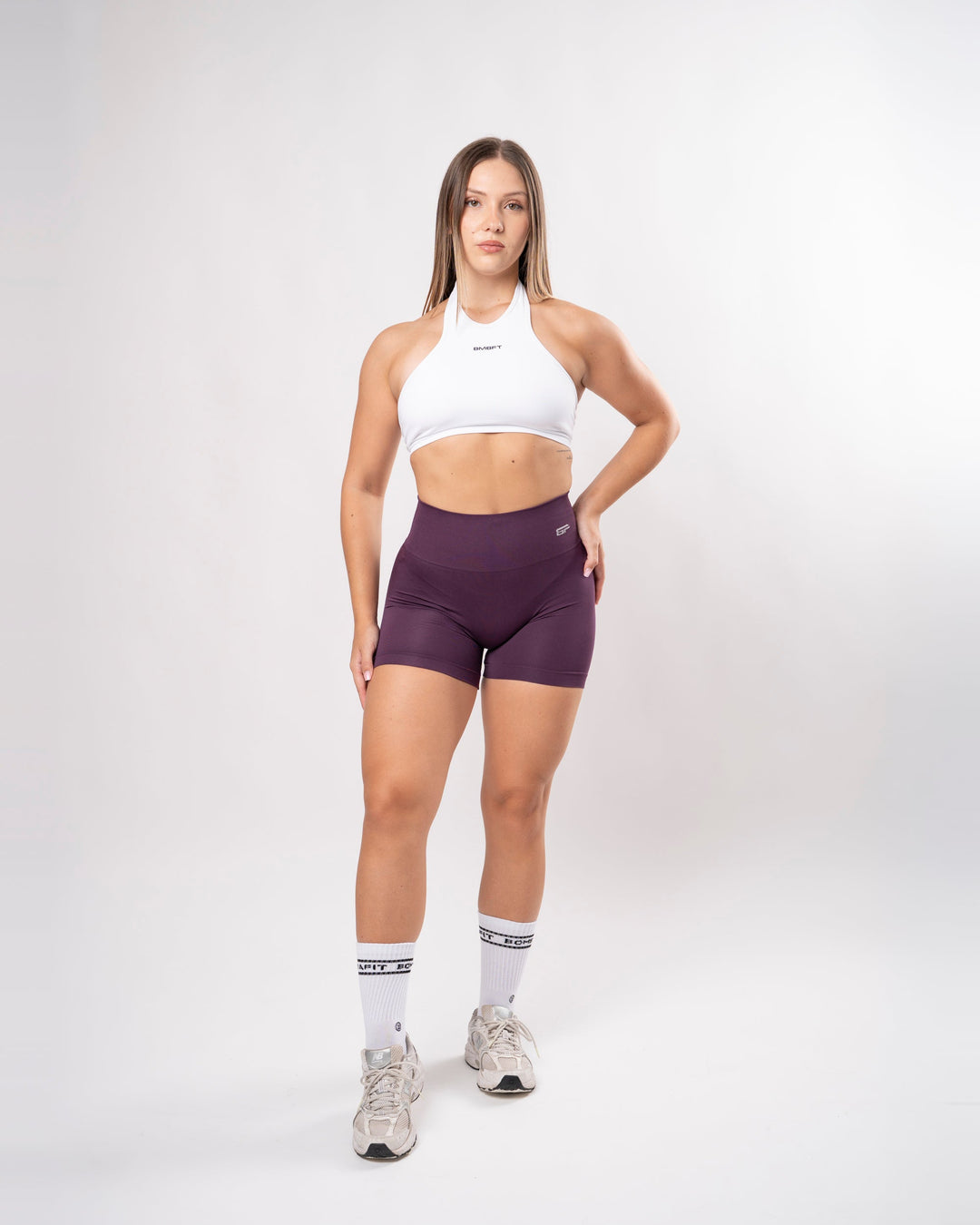 Modella indossa shorts sportivi seamless Bombafit color viola plum a vita alta con top bianco in studio