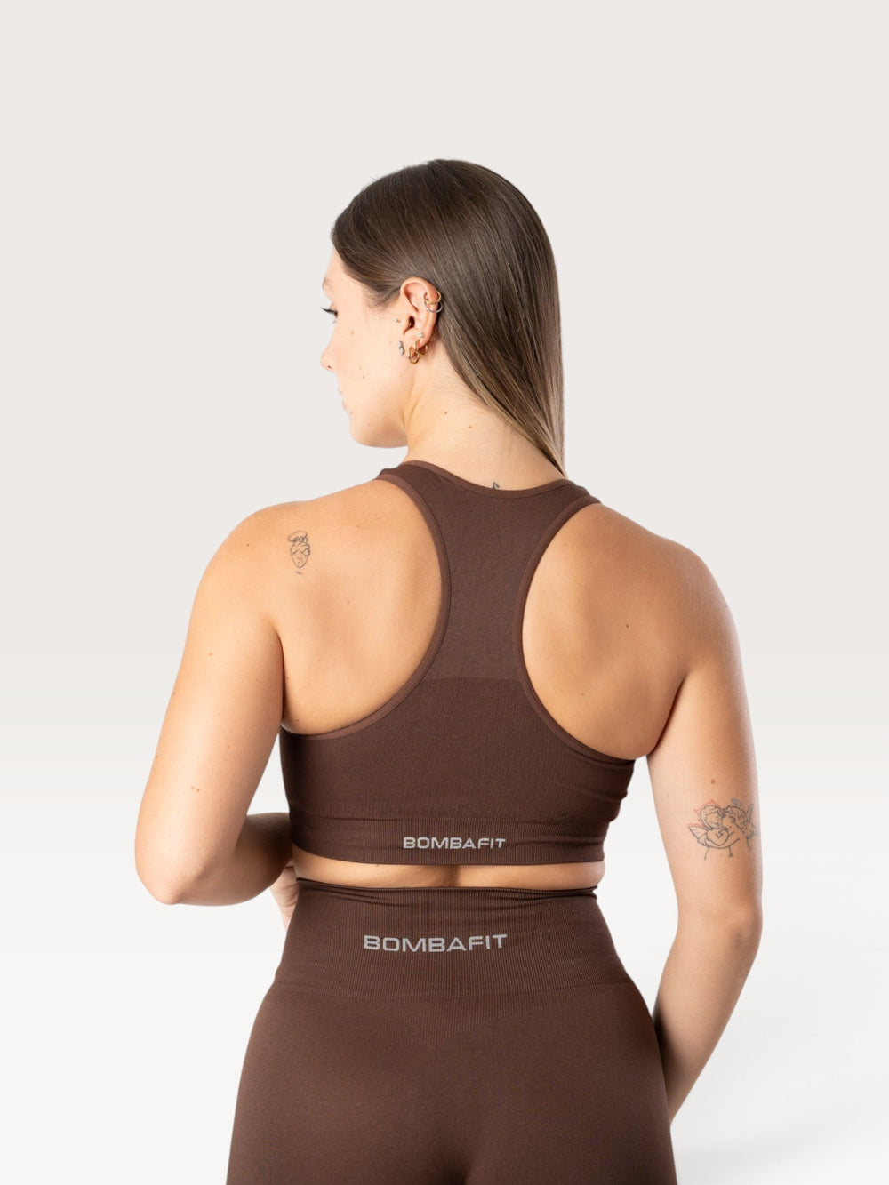 Modella di spalle indossa un top sportivo Bombafit marrone senza cuciture con design a vogatore