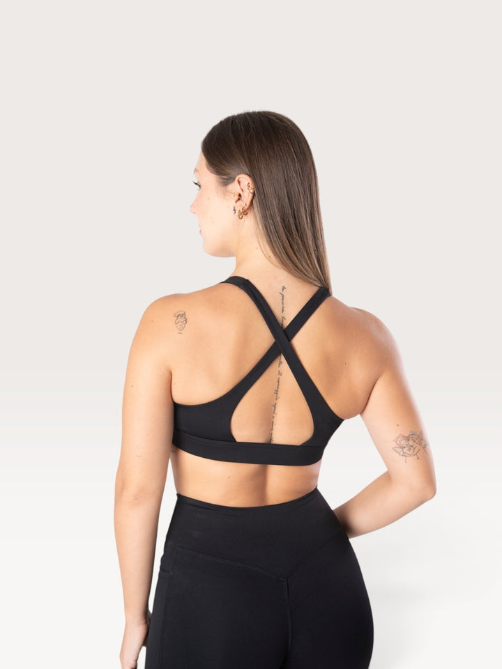 Modella di spalle indossa il top sportivo nero Bombafit Sense con spalline incrociate e fascia sottoseno